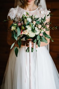 Bridal bouquet. Wedding. The girl in a white dress standing on a brown background and holds a beautiful bouquet of white, yellow, pink flowers and greenery, decorated with long silk ribbon.