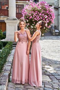 Beautiful blonde and brunette bridesmaids with luxury hairdo in gorgeous elegant stylish pale pink floor length v neck chiffon gown dress decorated with sequins sparkles and rhinestones on flowers background. Wedding day in old beautiful European city.
