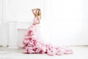 Dreamy woman portrait in a long pale pink ruffled gown in a white room.
